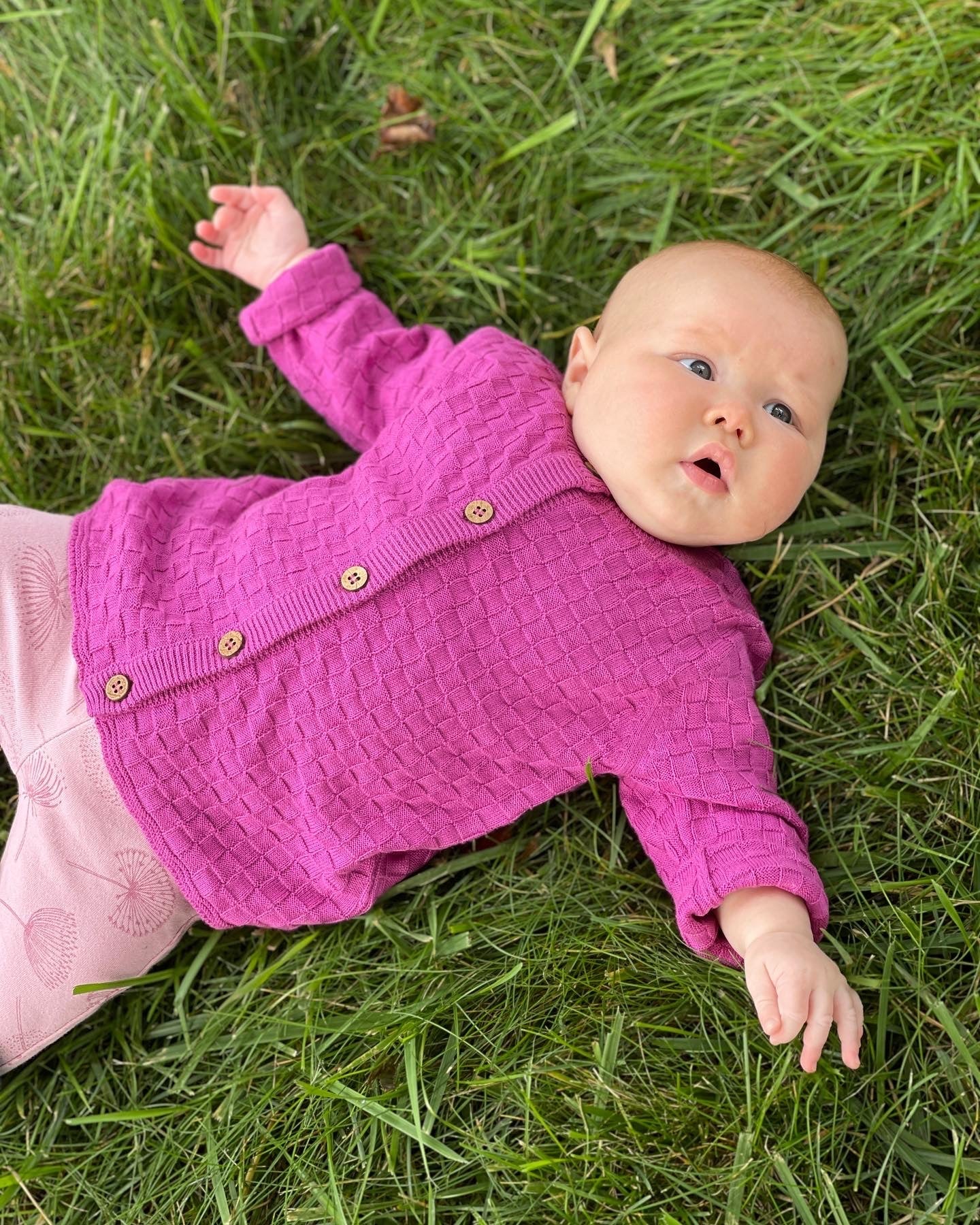 Baby in Bubblegum pink cardigan with wood buttons laying on grass 
