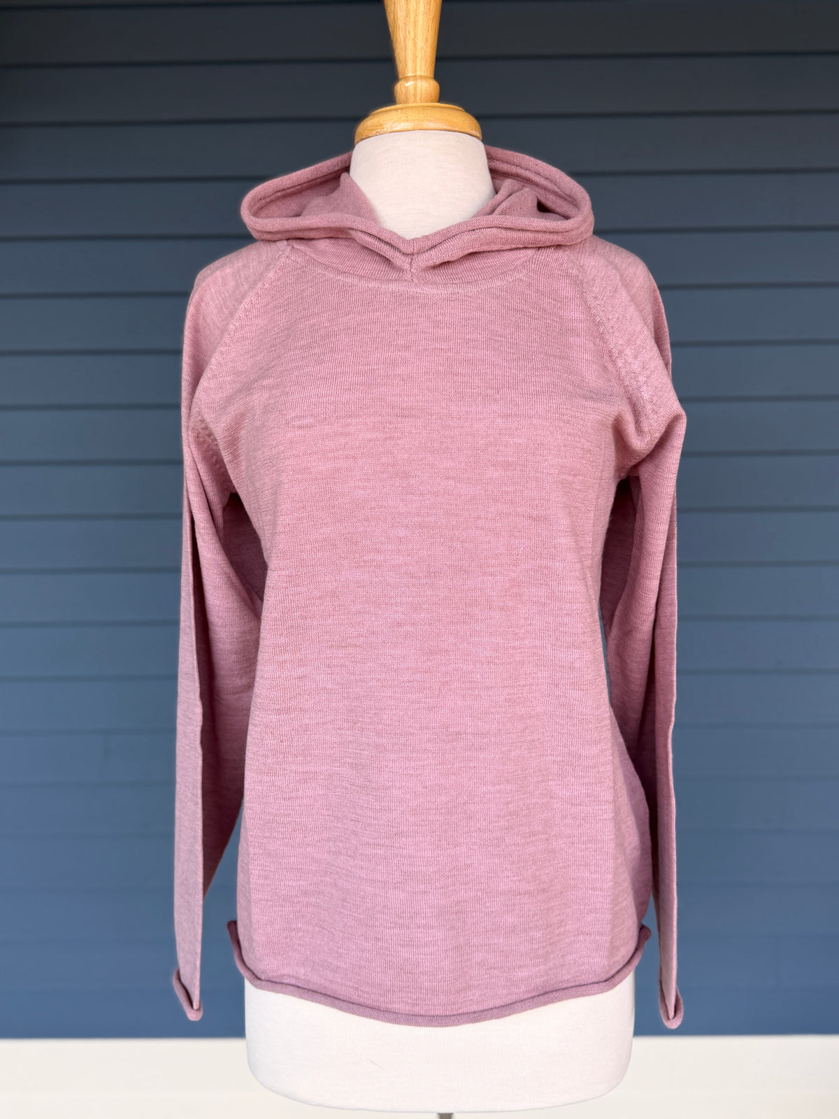 raglan sleeve hooded sweater with rolled edges in pink on mannequin in front of blue and cream colored building.