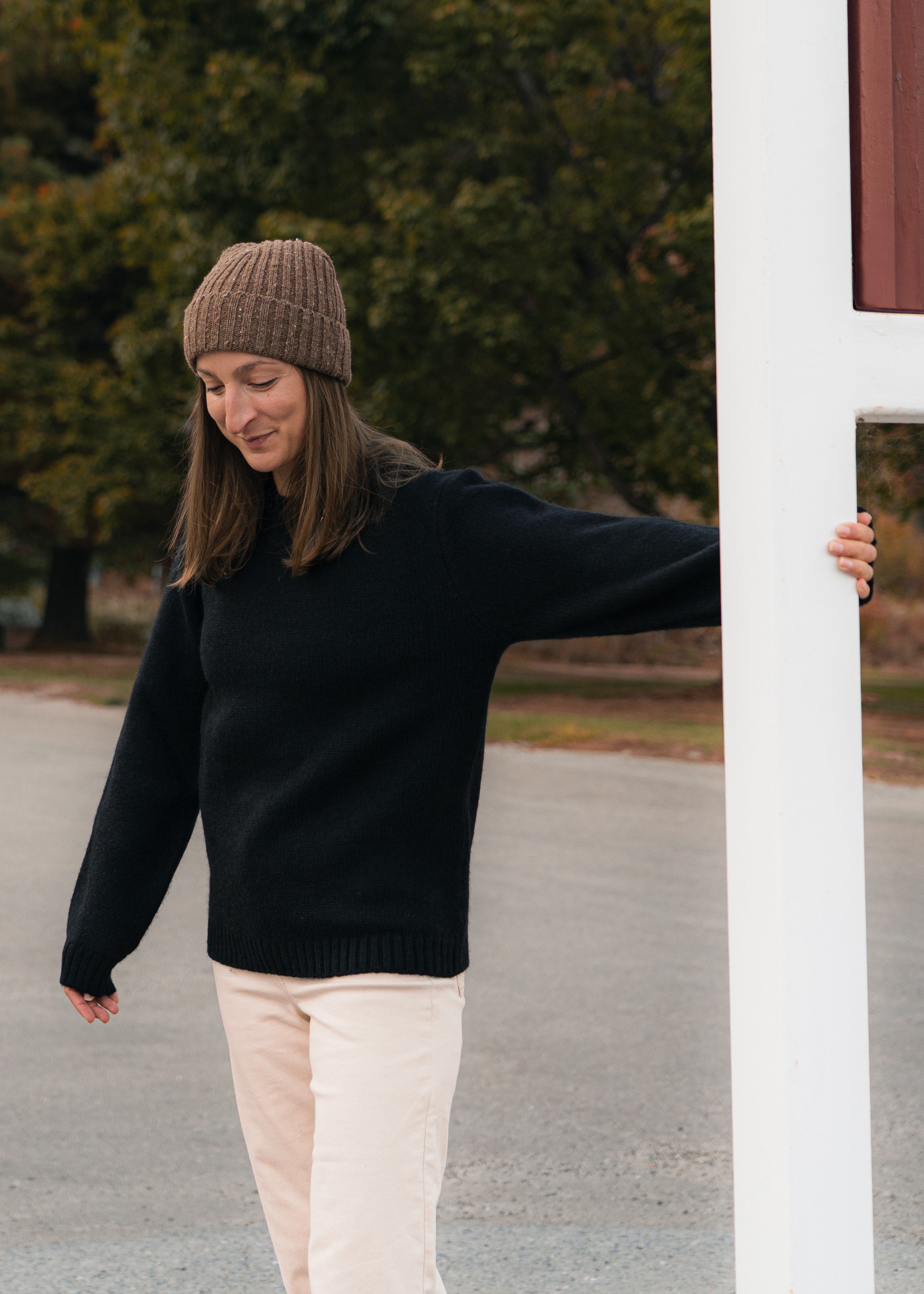 Woman wearing a black Black Bear sweater and beige beanie standing next to a white pole outdoors.