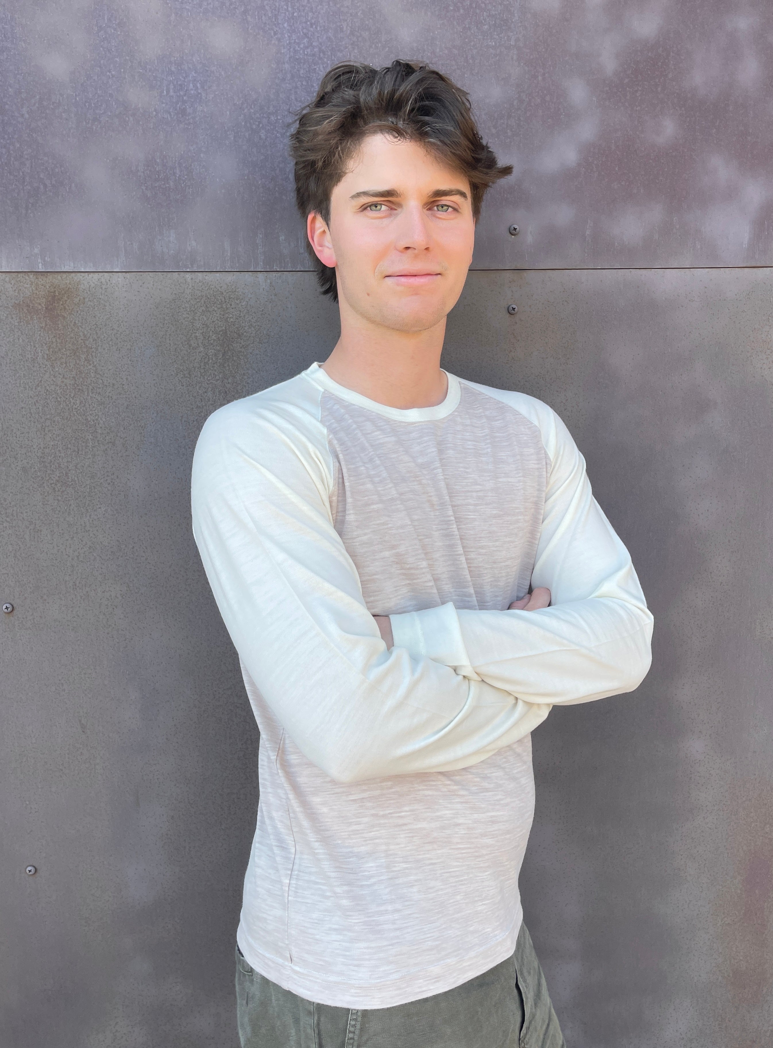 Man wearing a light gray long-sleeve Home Team shirt against a textured gray wall