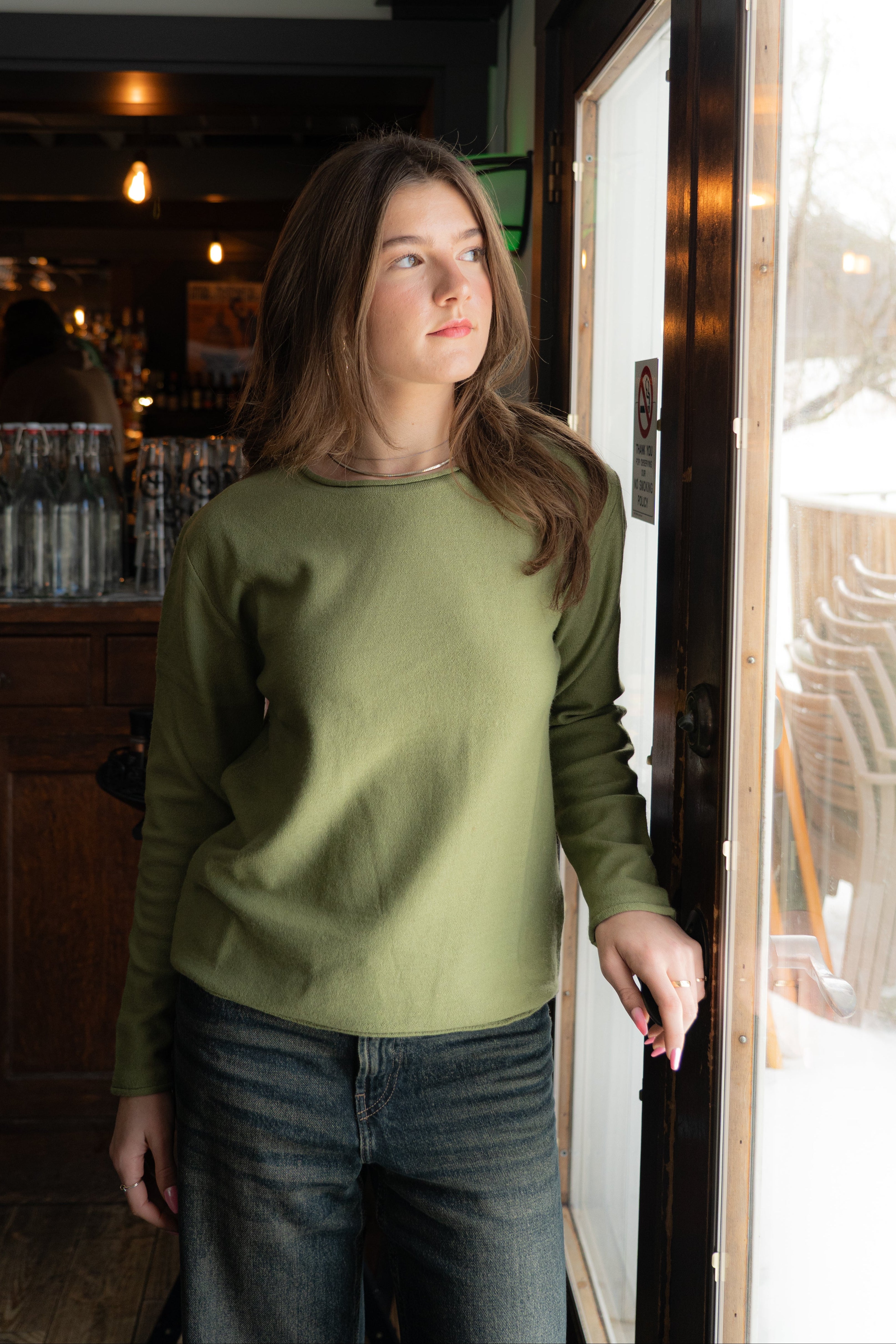 Woman in a green sweater standing by a door inside a bar.