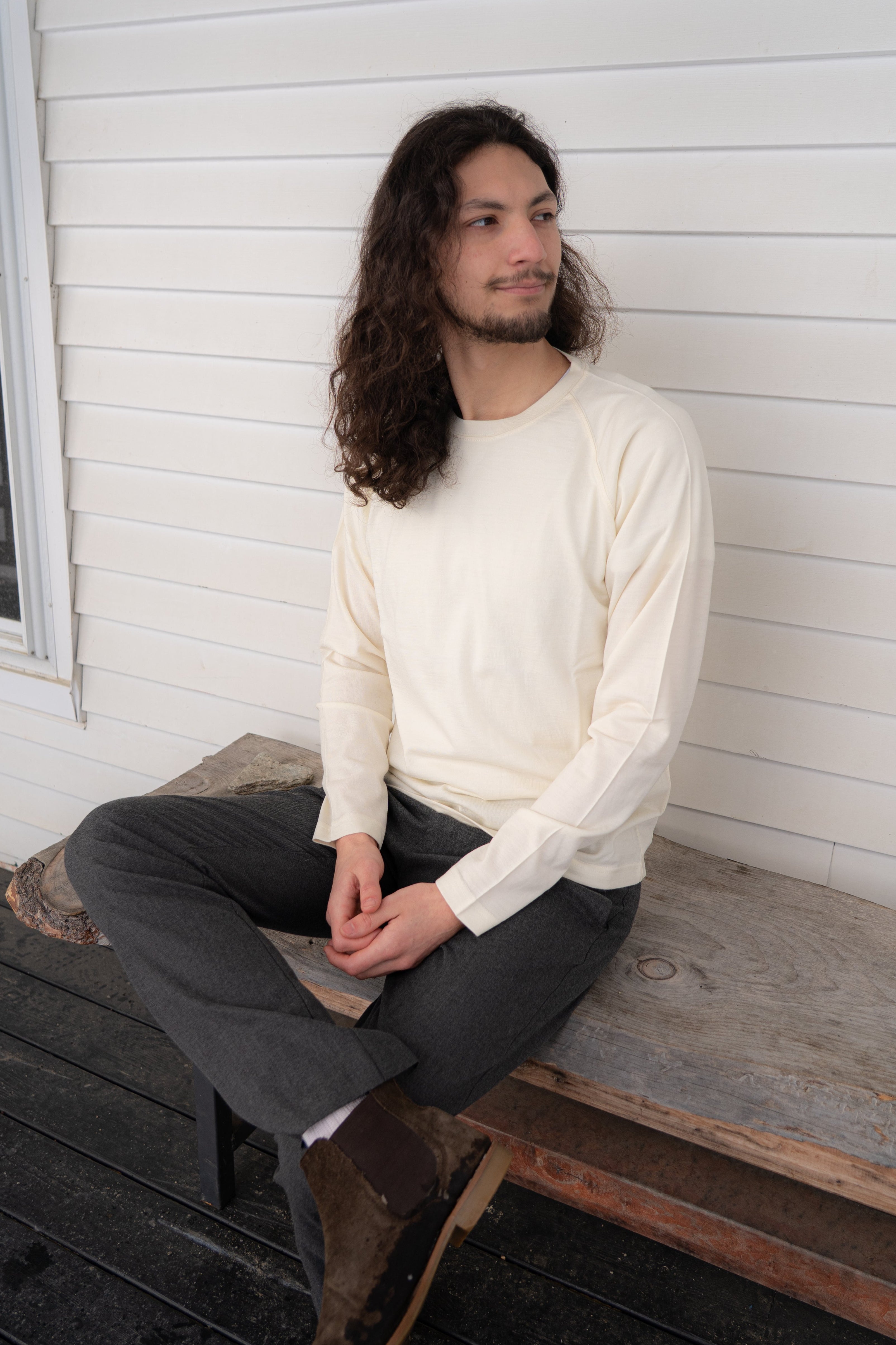 Man sitting on a wooden bench against a white wall