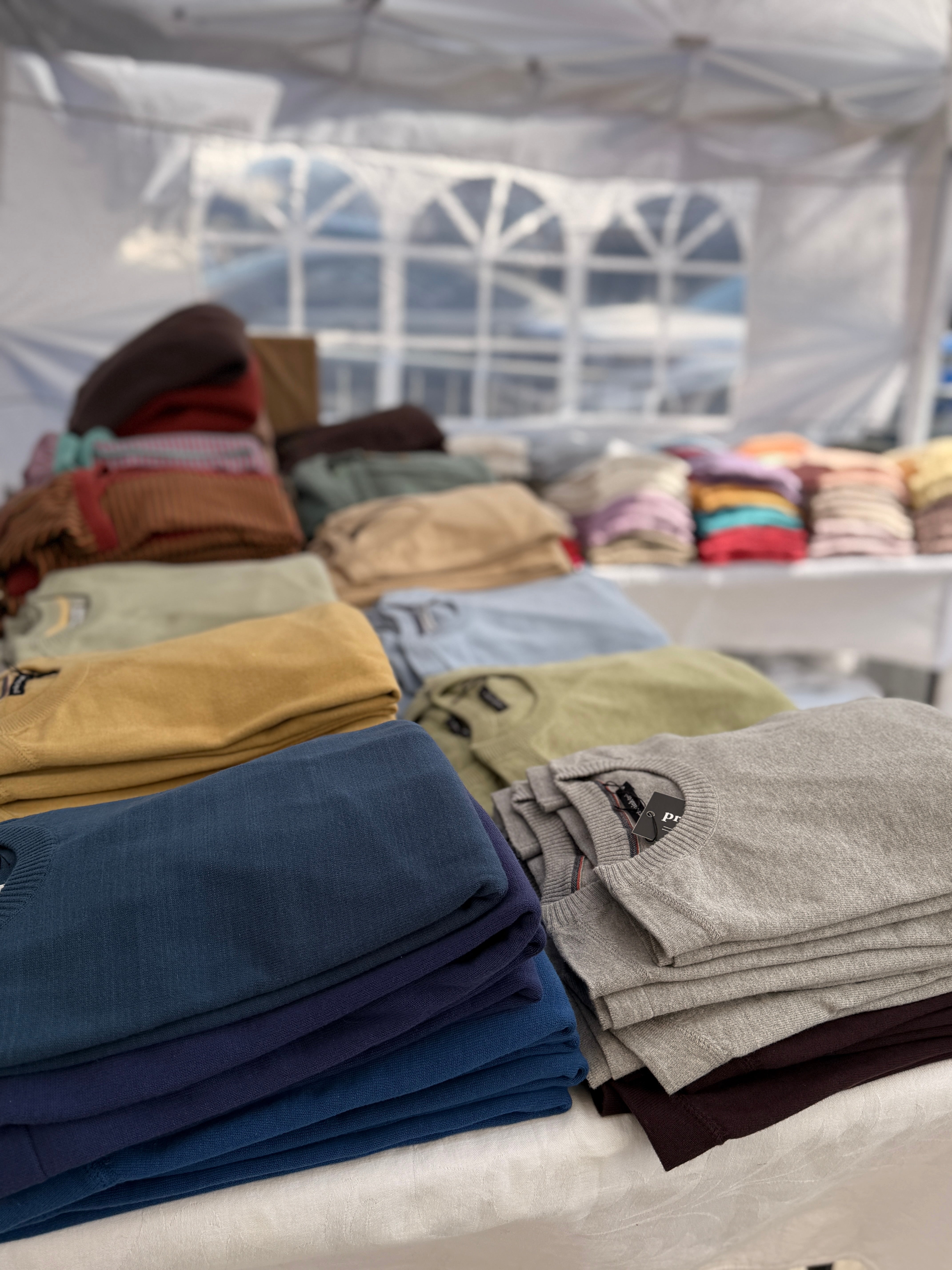 piles of sweaters in a pop up tent showing my booth set up