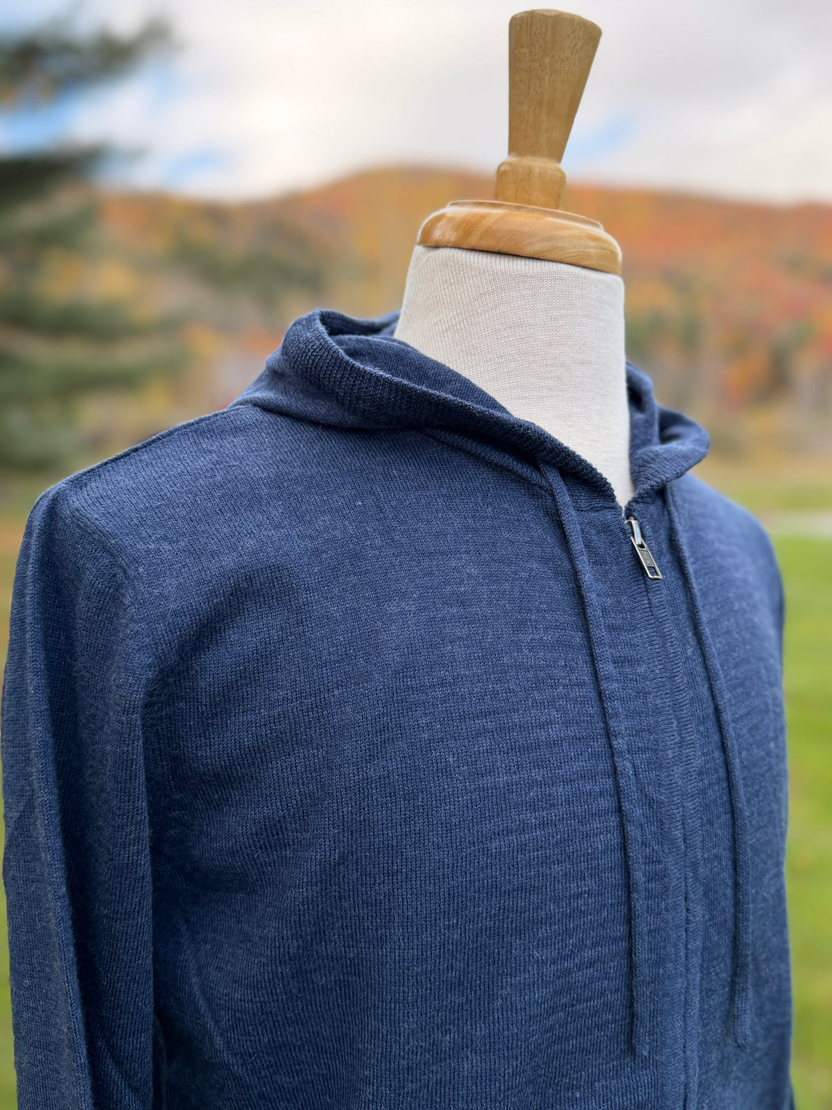 Close up photo of hoodie on mannequin in blue color with fall foliage in the background
