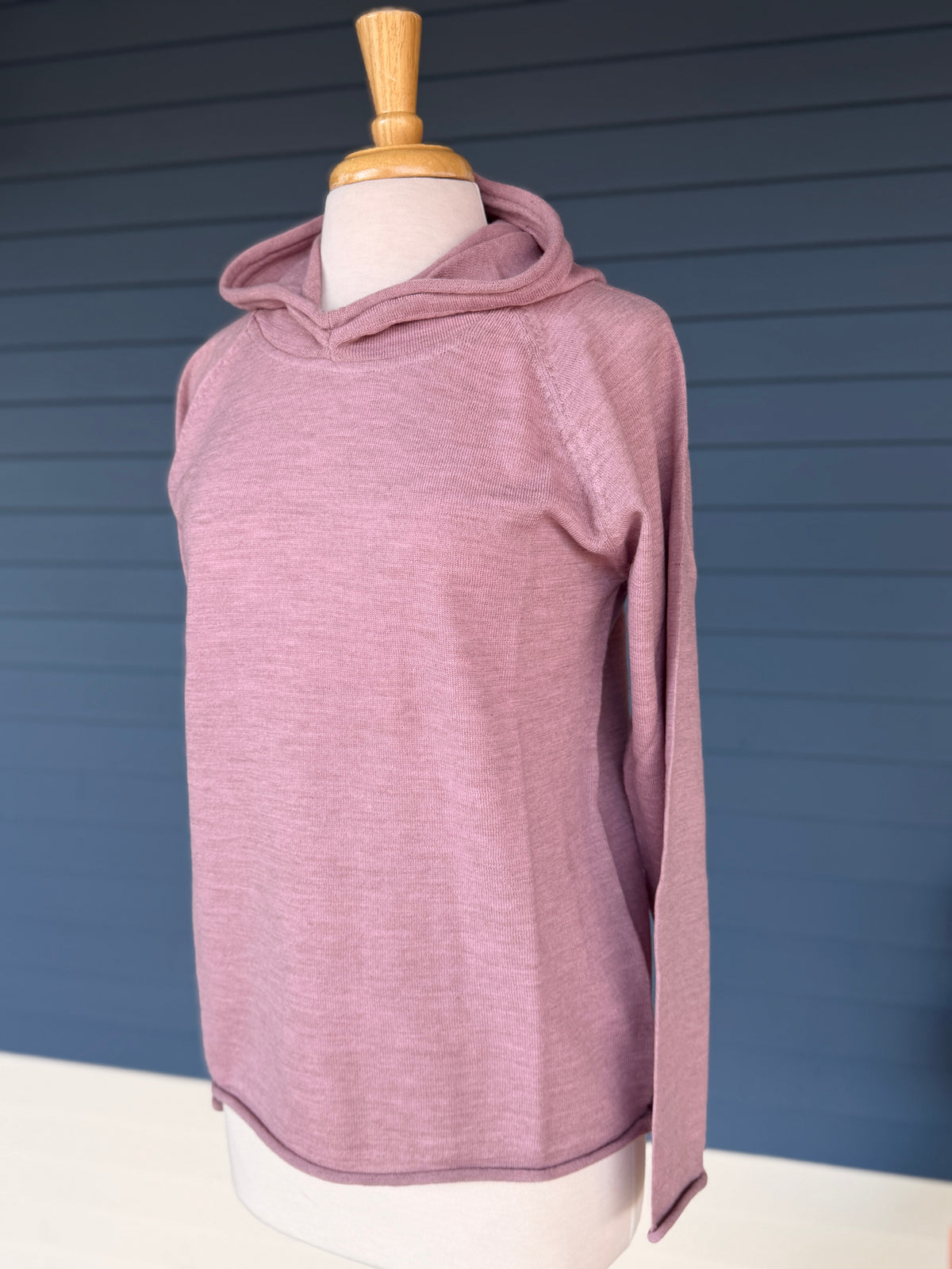 Pink raglan sleeve hooded sweater on mannequin in front of blue building. 